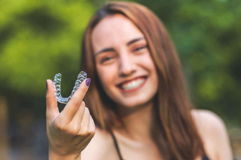 Beautiful smiling Turkish woman is holding an invisalign bracer with vibrant colors